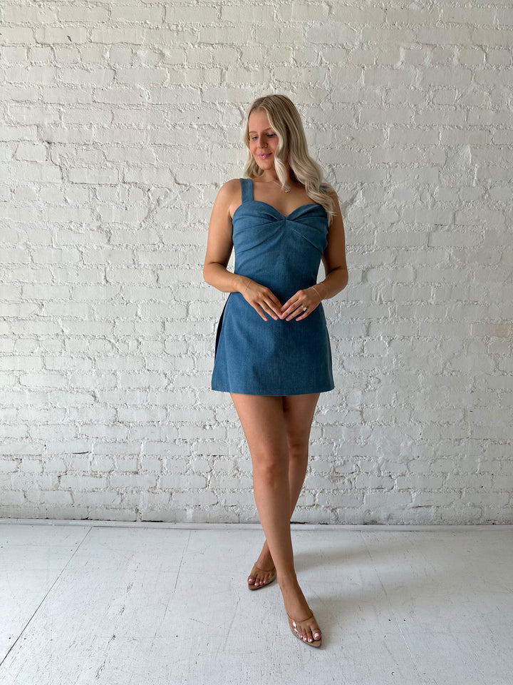 Woman wearing medium wash denim mini dress with built in shorts, and sweetheart neckline. 