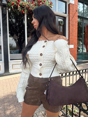 Woman wearing ivory long sleeve off the shoulder button up cardigan and brown suede shorts. 
