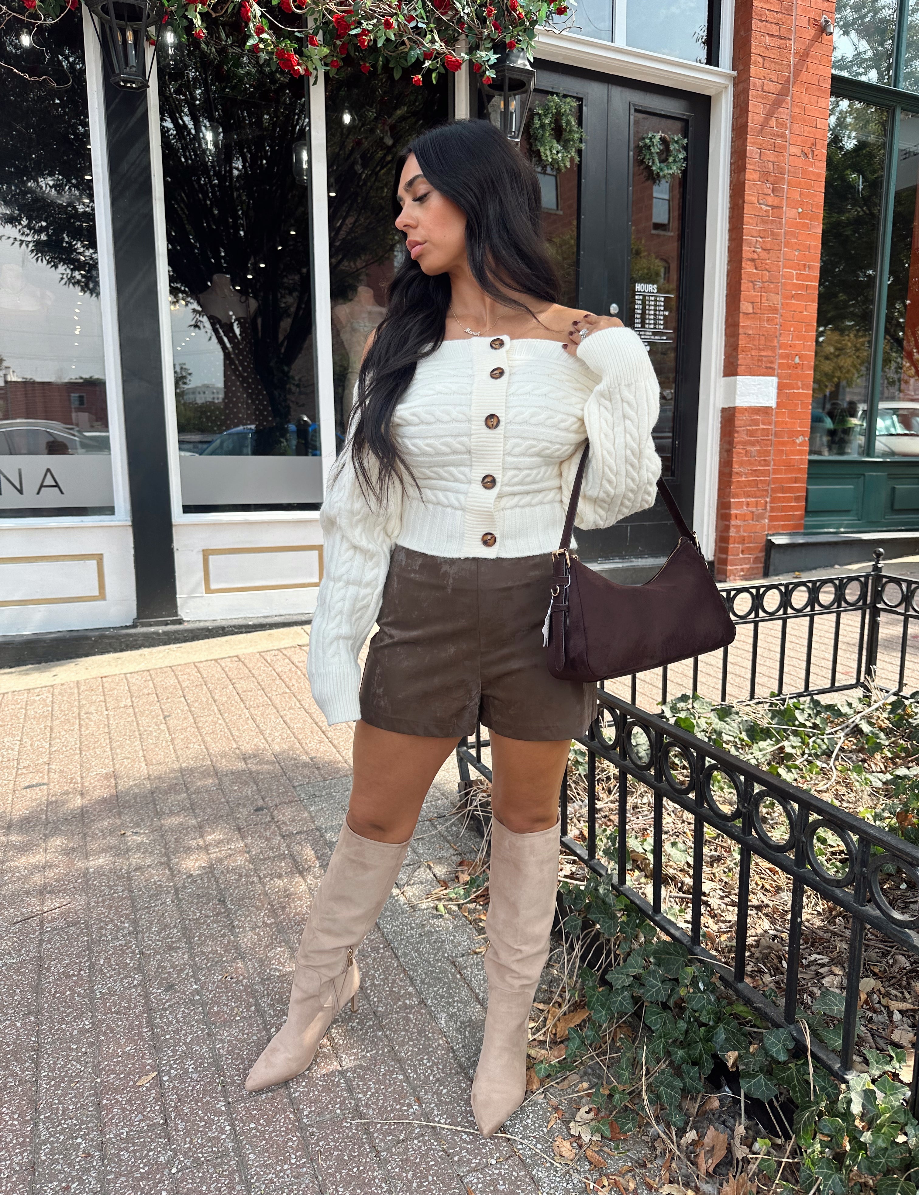 Woman wearing ivory long sleeve off the shoulder button up cardigan and brown suede shorts. 