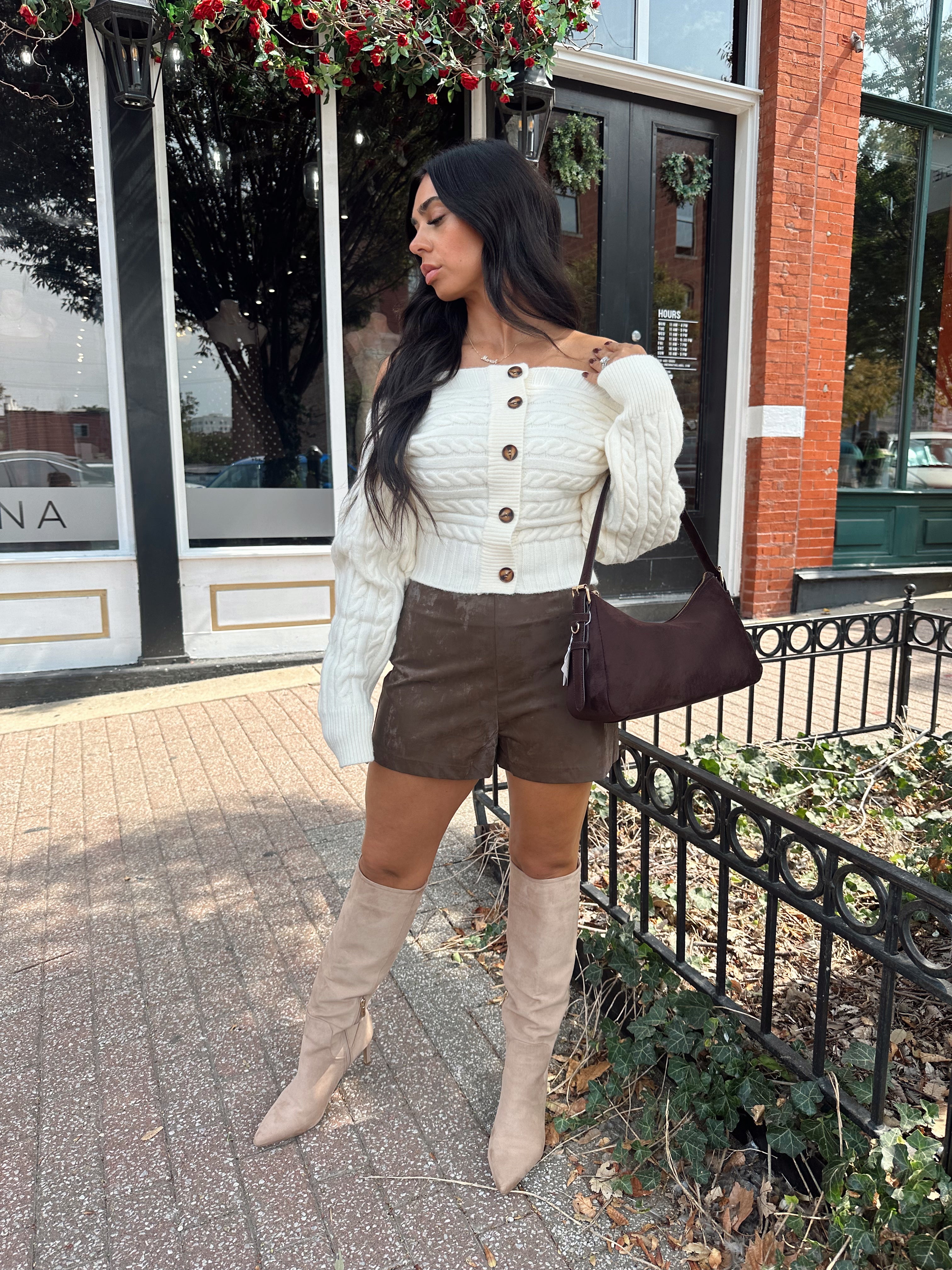 Woman wearing ivory long sleeve off the shoulder button up cardigan and brown suede shorts. 