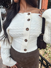 Woman wearing ivory long sleeve off the shoulder button up cardigan and brown suede shorts. 