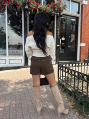 Woman wearing ivory long sleeve off the shoulder button up cardigan and brown suede shorts. 