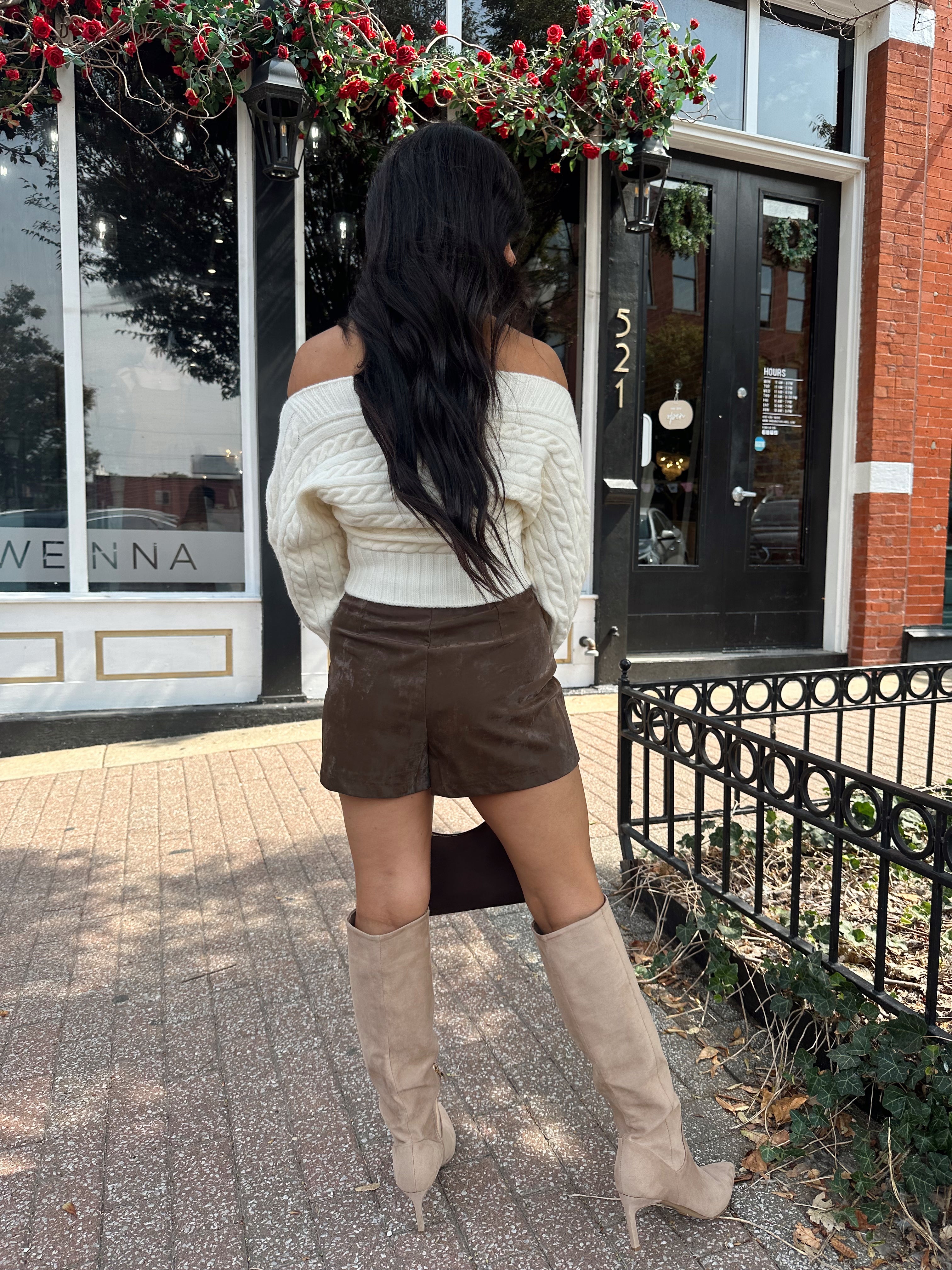 Woman wearing ivory long sleeve off the shoulder button up cardigan and brown suede shorts. 