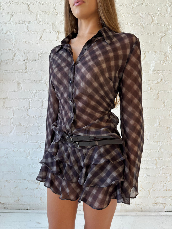 Woman wearing sheer brown plaid two piece ruffle skirt set with belted waist and tie detail.