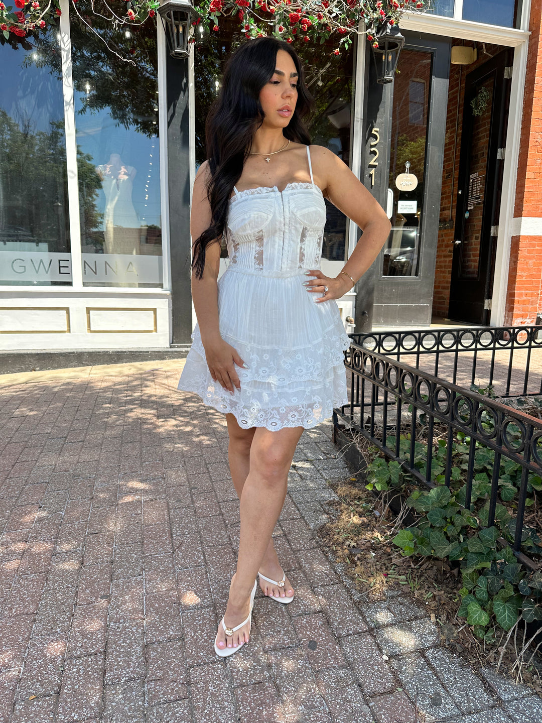 Woman wearing whiter tiered mini dress with lace detailing, and clasp closure. 