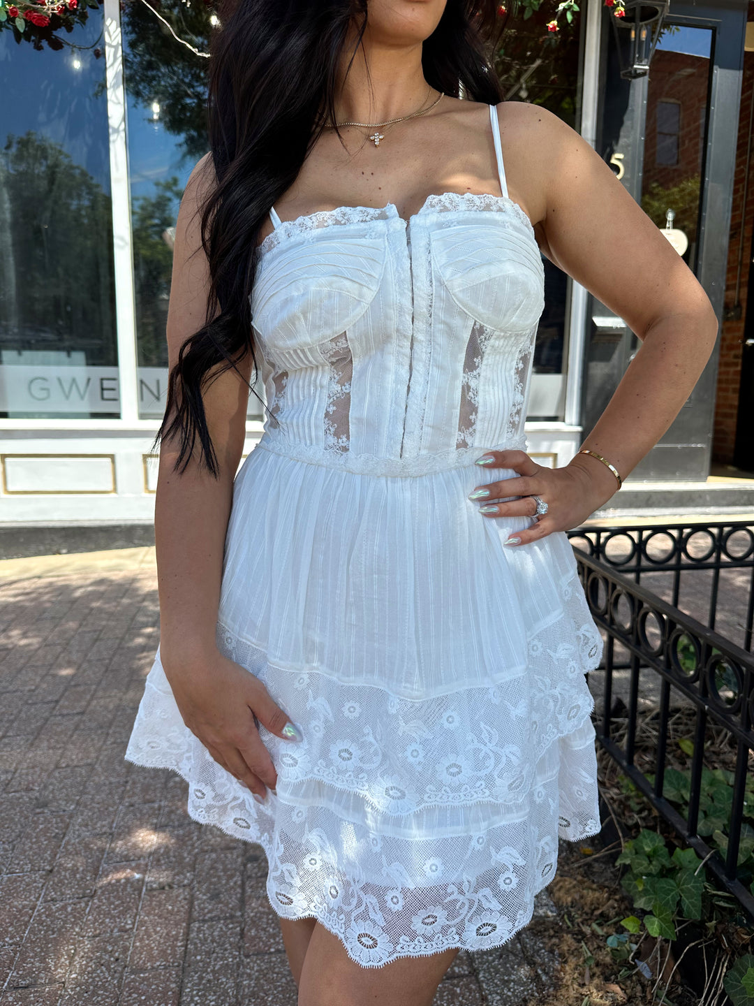 Woman wearing whiter tiered mini dress with lace detailing, and clasp closure. 