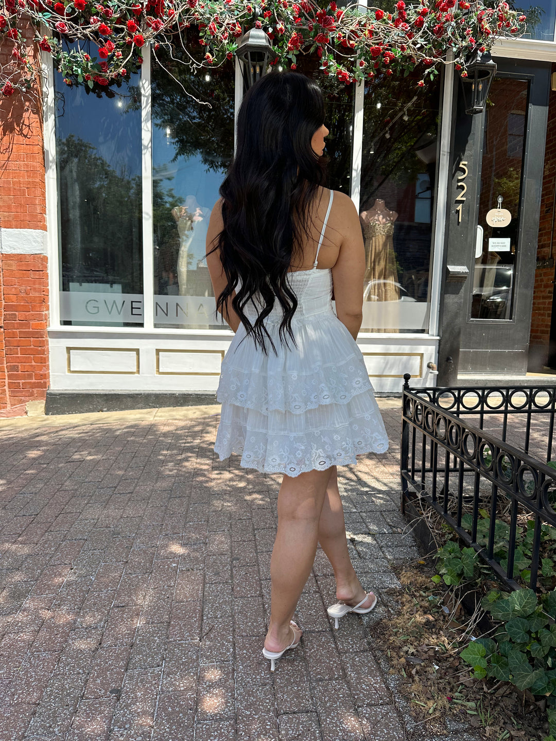 Woman wearing whiter tiered mini dress with lace detailing, and clasp closure. 
