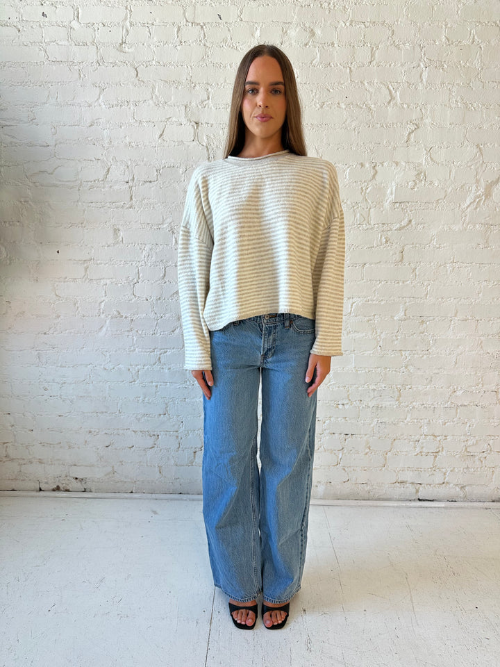 Woman wearing beige and ivory striped knit pull over sweater with medium wash jeans. 