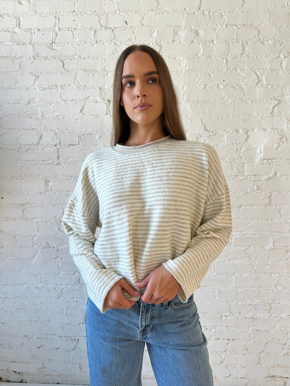Woman wearing beige and ivory striped knit pull over sweater with medium wash jeans. 