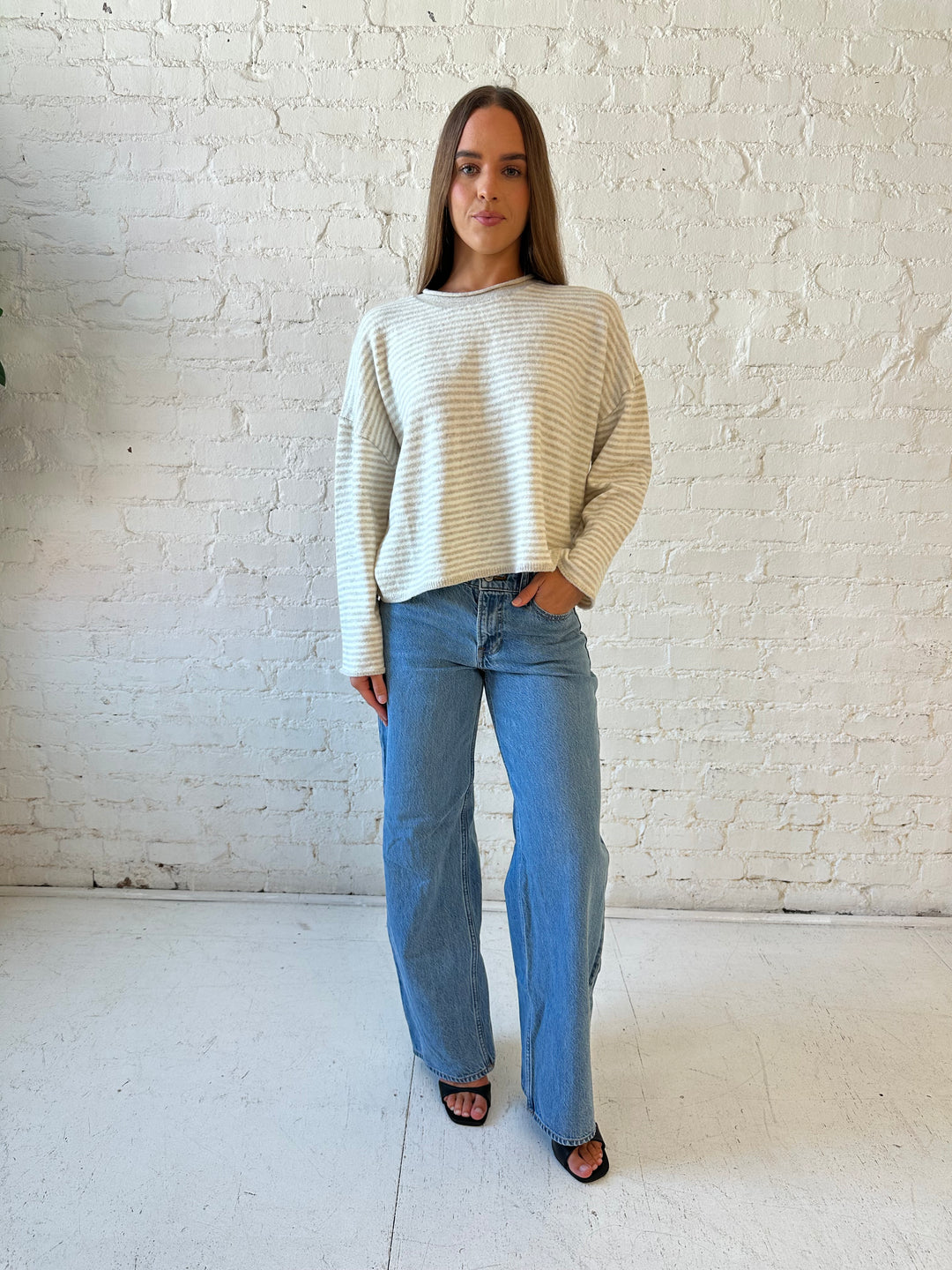Woman wearing beige and ivory striped knit pull over sweater with medium wash jeans. 