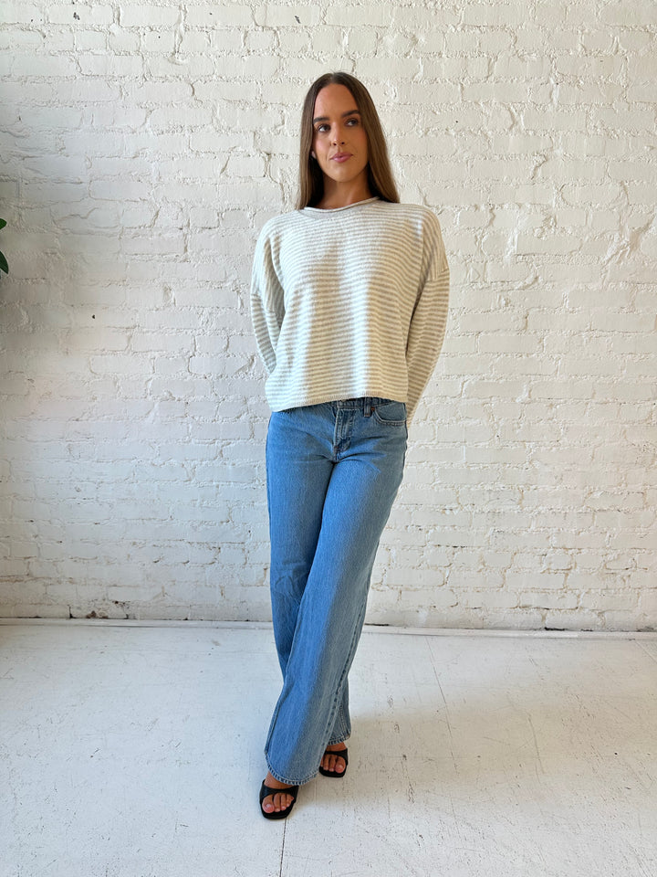 Woman wearing beige and ivory striped knit pull over sweater with medium wash jeans. 