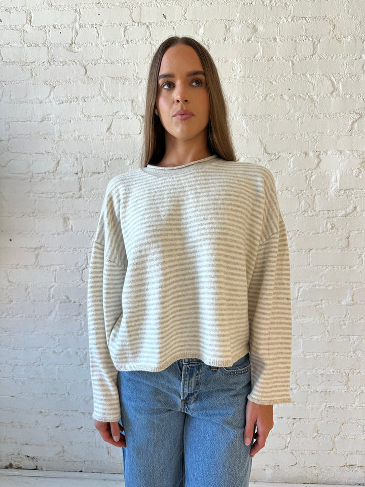 Woman wearing beige and ivory striped knit pull over sweater with medium wash jeans. 
