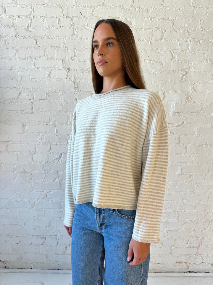 Woman wearing beige and ivory striped knit pull over sweater with medium wash jeans. 