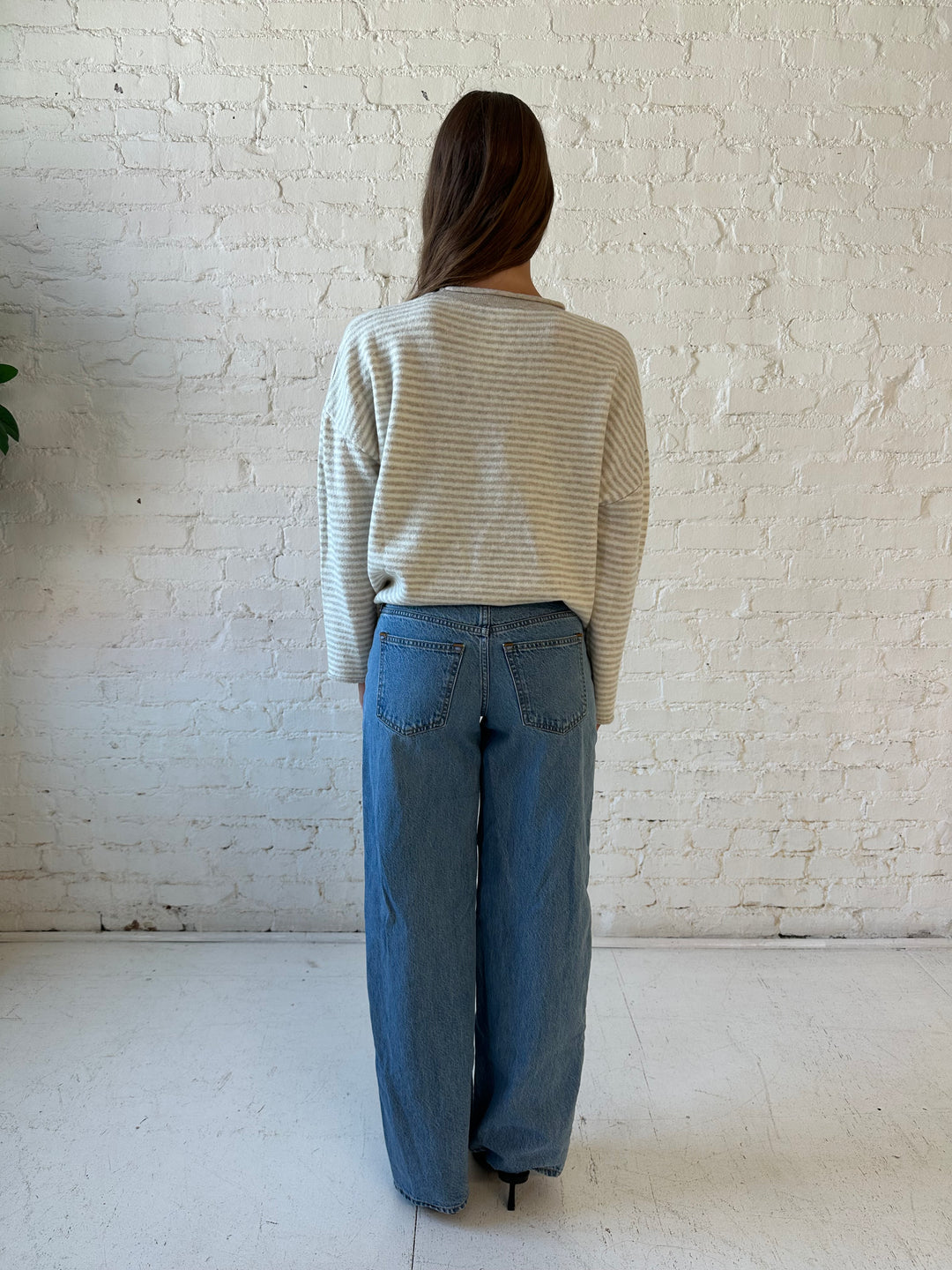 Woman wearing beige and ivory striped knit pull over sweater with medium wash jeans. 
