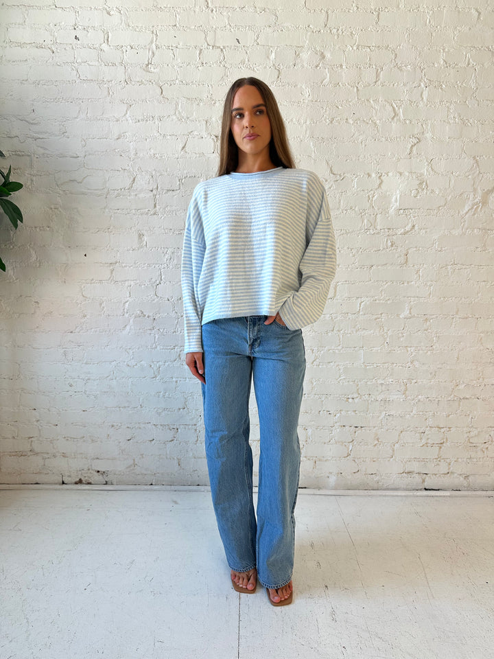 Woman wearing ivory and blue knit pull over sweater with medium wash jeans. 