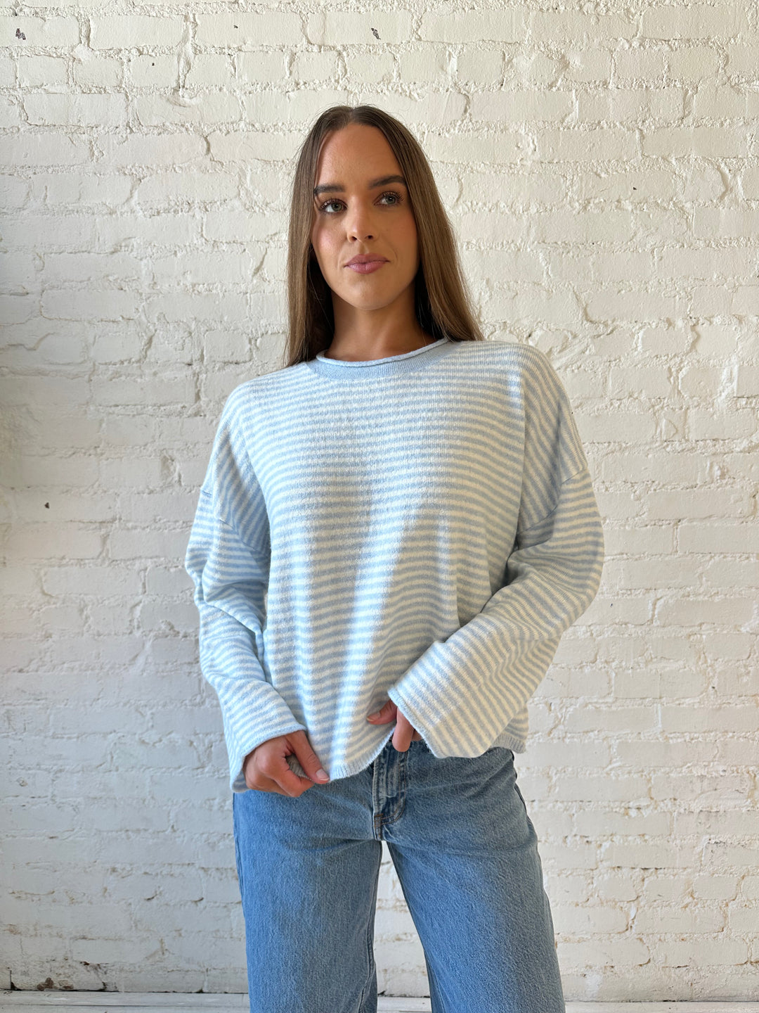 Woman wearing ivory and blue knit pull over sweater with medium wash jeans. 