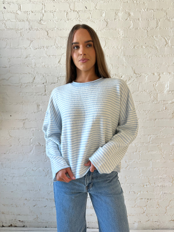 Woman wearing ivory and blue knit pull over sweater with medium wash jeans. 