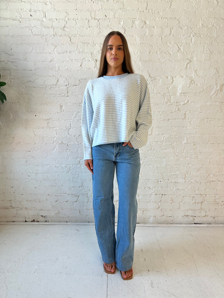 Woman wearing ivory and blue knit pull over sweater with medium wash jeans. 