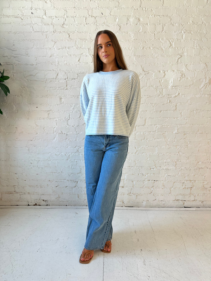 Woman wearing ivory and blue knit pull over sweater with medium wash jeans. 