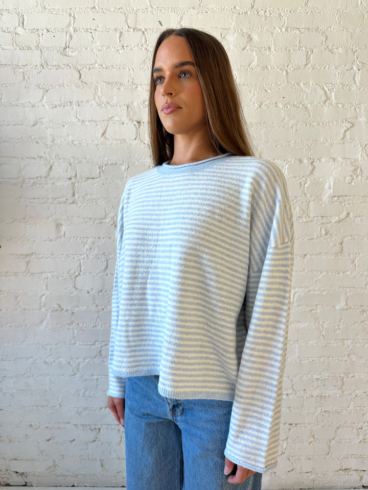 Woman wearing ivory and blue knit pull over sweater with medium wash jeans. 
