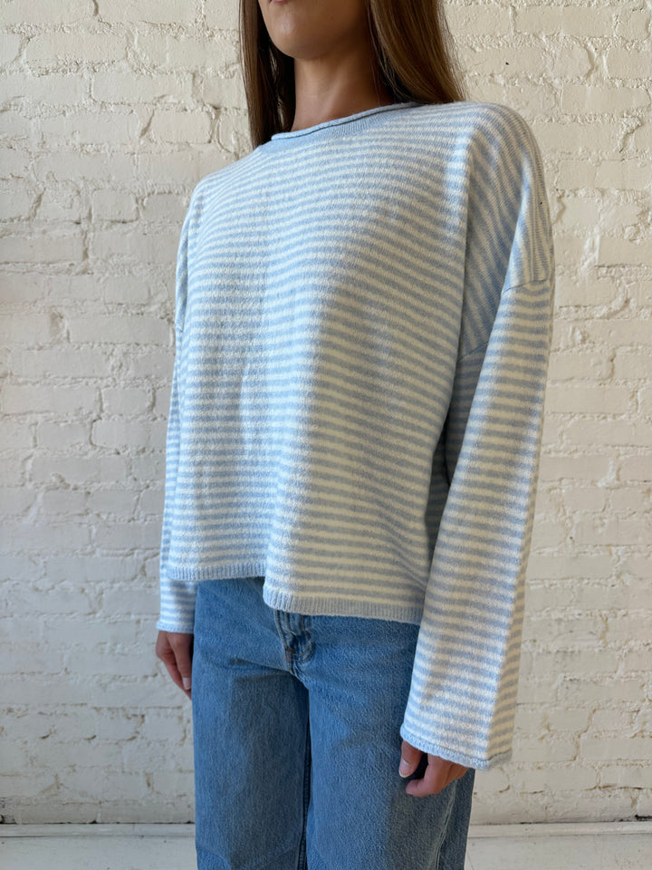 Woman wearing ivory and blue knit pull over sweater with medium wash jeans. 