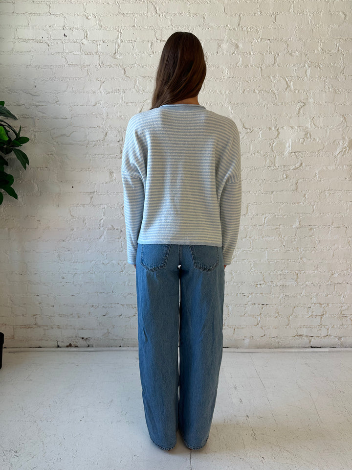 Woman wearing ivory and blue knit pull over sweater with medium wash jeans. 