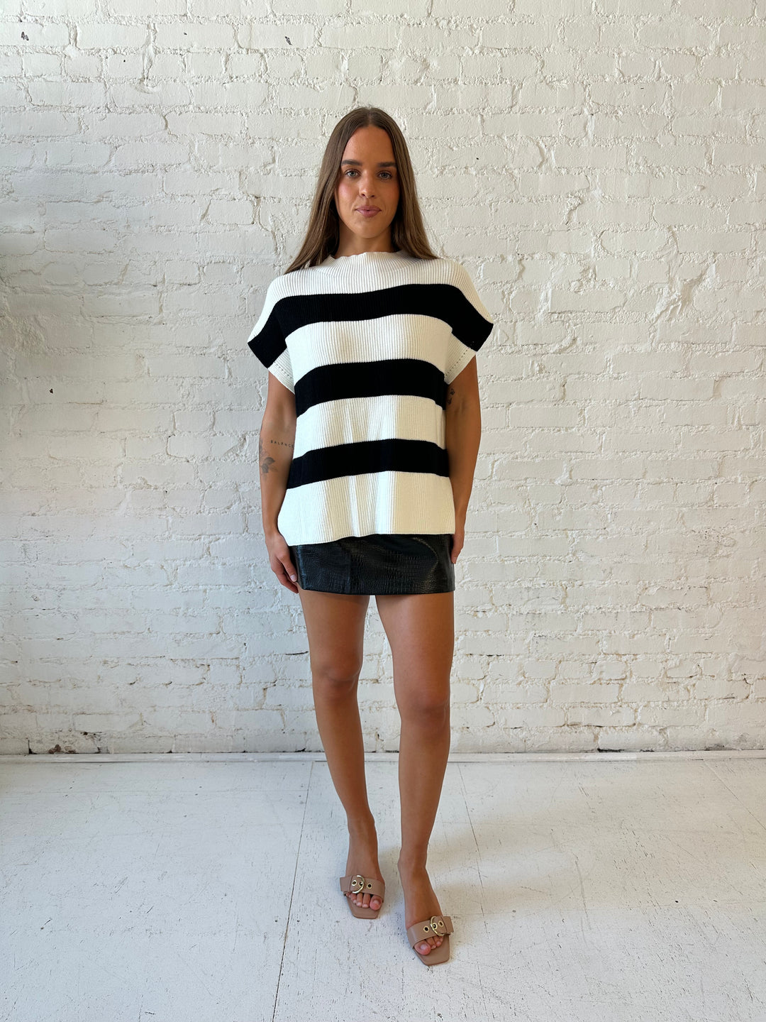 Woman wearing black and white chunky oversized sweater with black faux leather skirt.