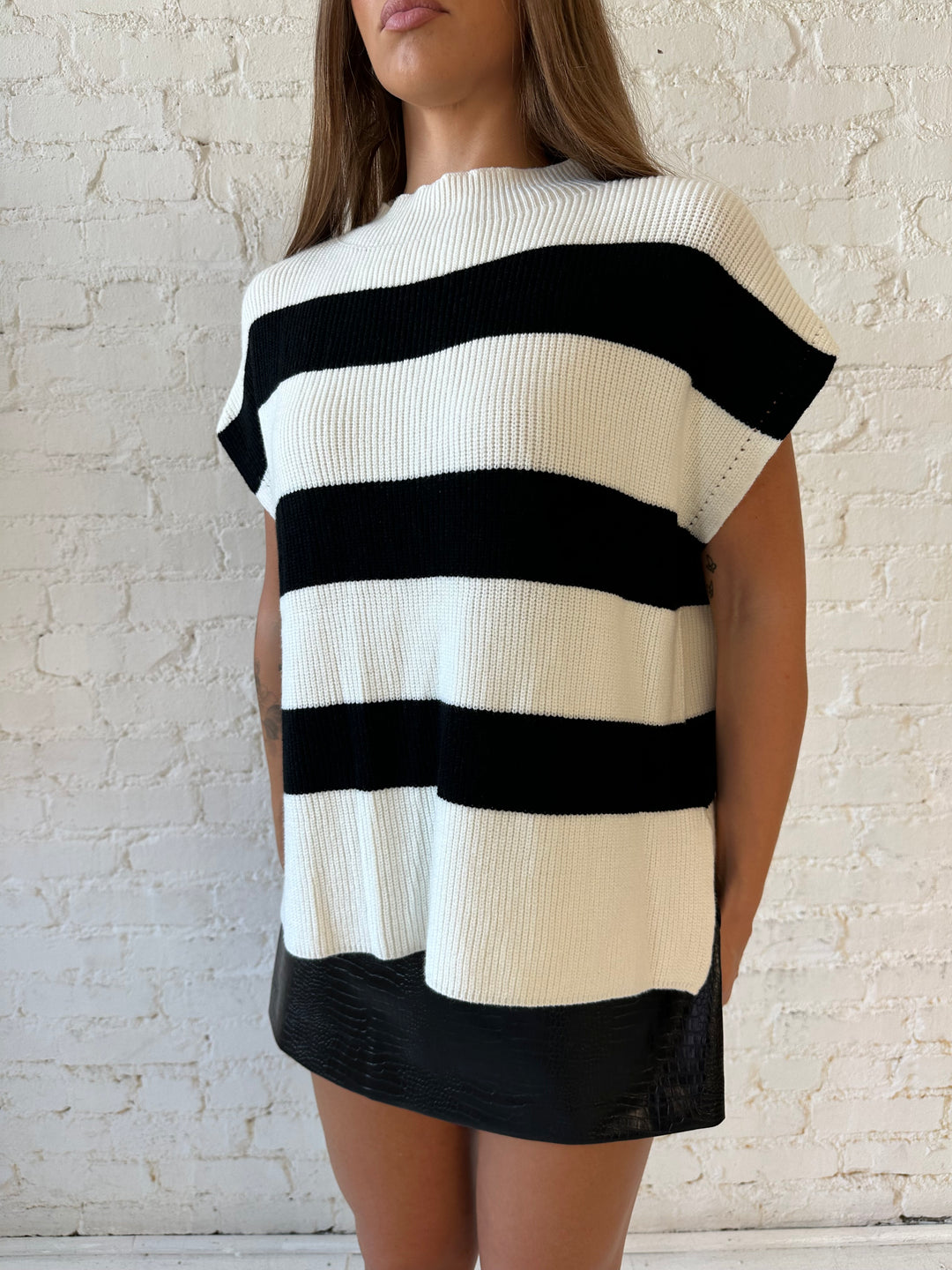 Woman wearing black and white chunky oversized sweater with black faux leather skirt.