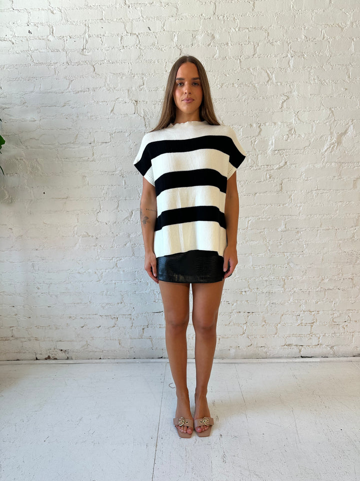 Woman wearing black and white chunky oversized sweater with black faux leather skirt.