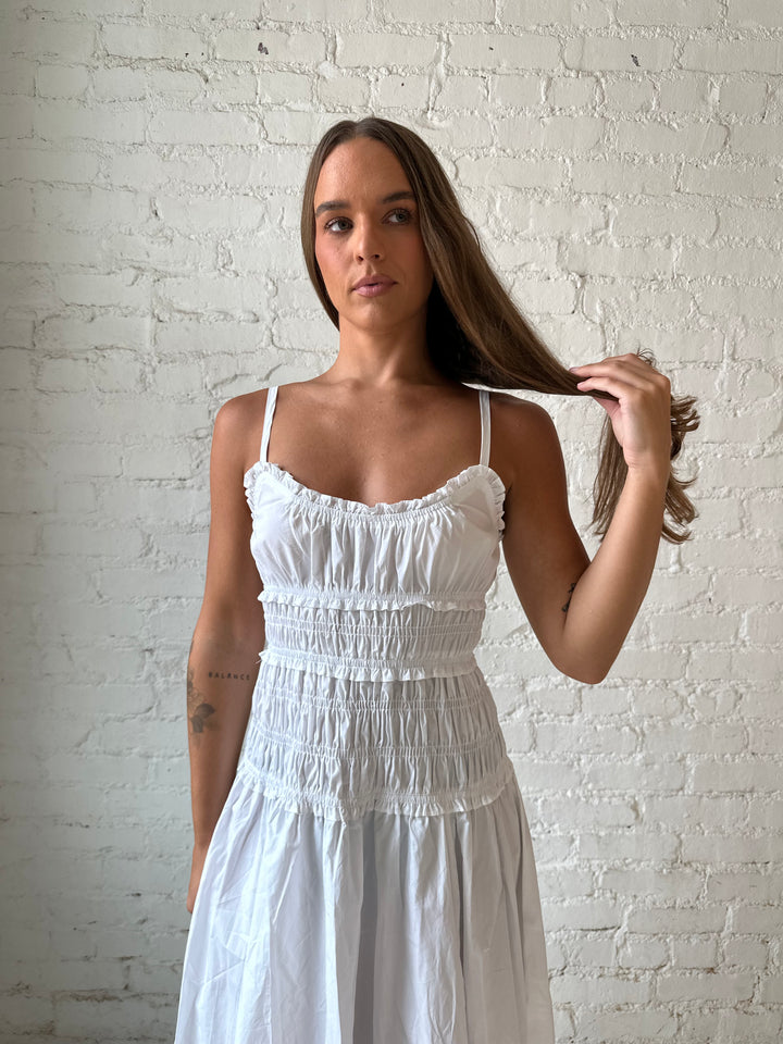 Woman wearing white smocked maxi dress with side slit. 
