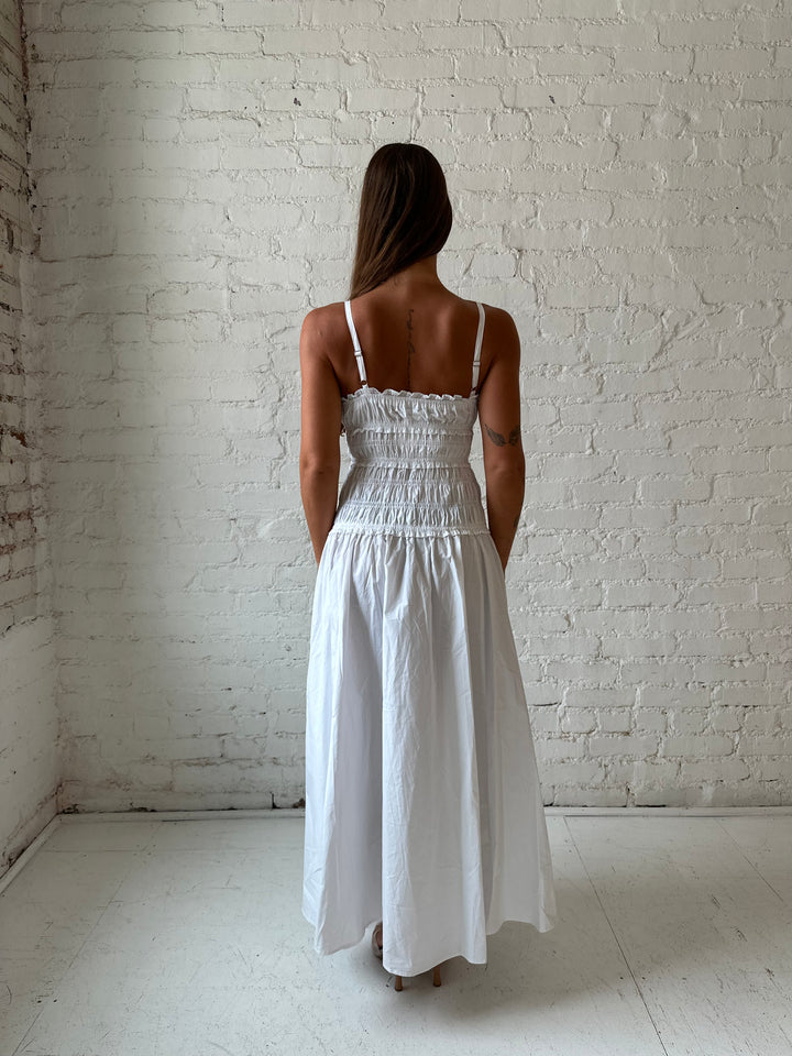Woman wearing white smocked maxi dress with side slit. 