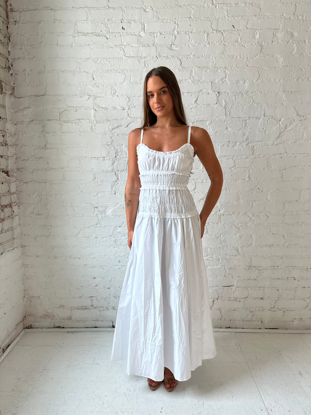 Woman wearing white smocked maxi dress with side slit. 