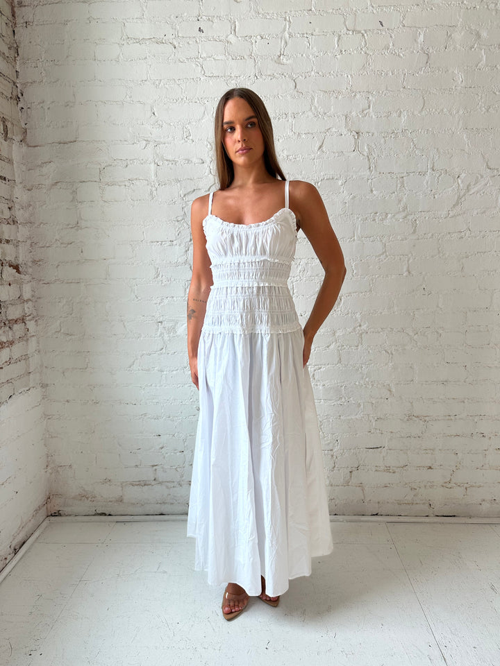 Woman wearing white smocked maxi dress with side slit. 