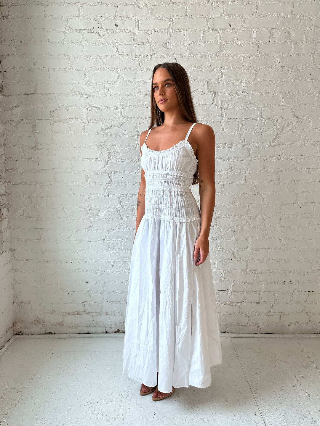 Woman wearing white smocked maxi dress with side slit. 