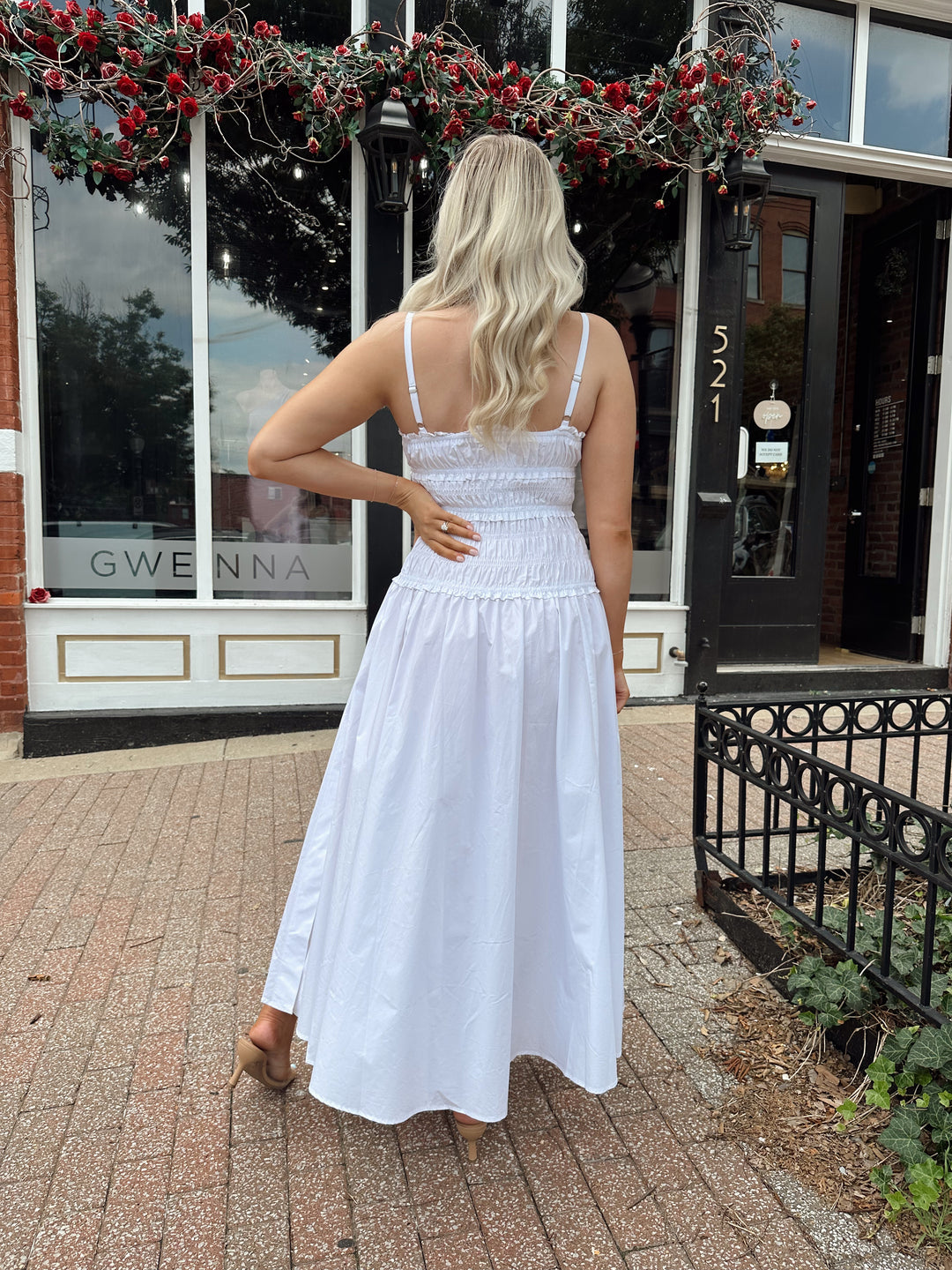 Woman wearing white smocked maxi dress with side slit. 