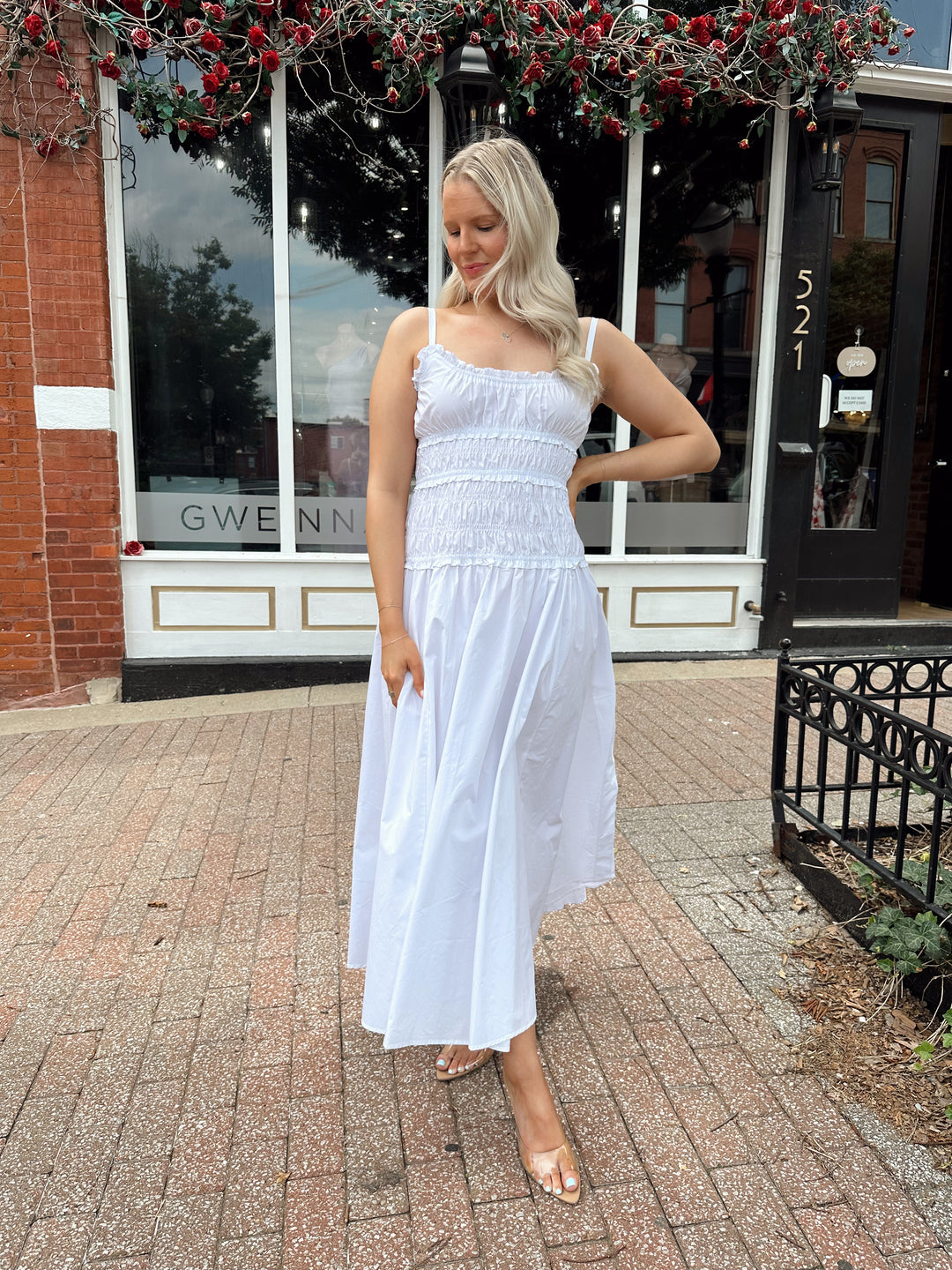 Woman wearing white smocked maxi dress with side slit. 