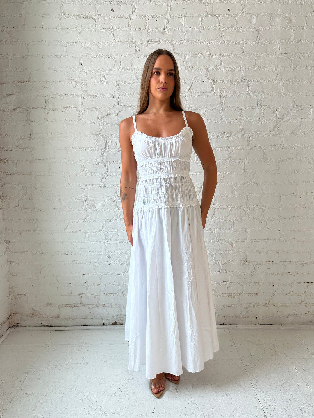 Woman wearing white smocked maxi dress with side slit. 