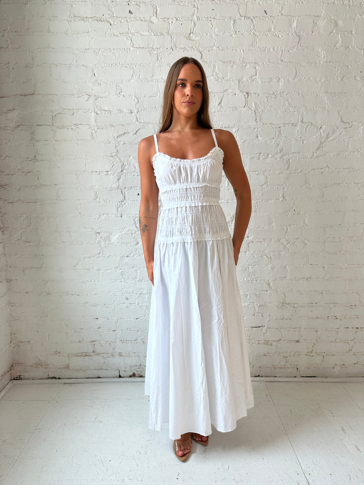 Woman wearing white smocked maxi dress with side slit. 