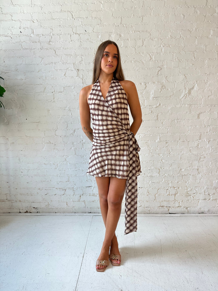 Woman wearing abstract print brown mini dress with wrap tie skirt and halter neckline.