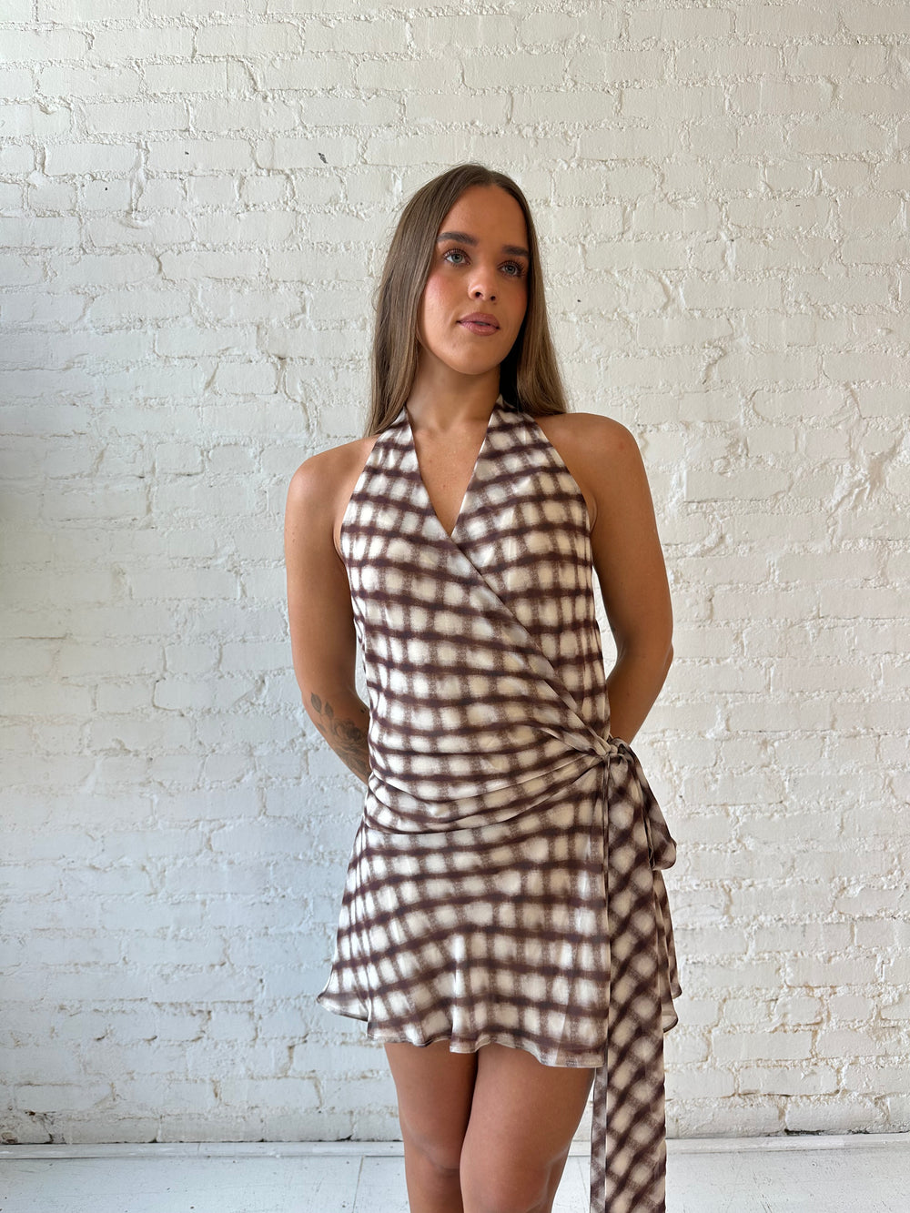 Woman wearing abstract print brown mini dress with wrap tie skirt and halter neckline.