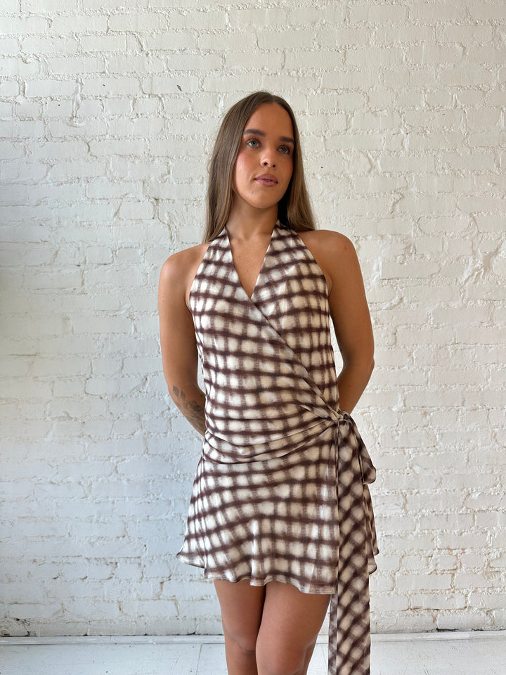 Woman wearing abstract print brown mini dress with wrap tie skirt and halter neckline.