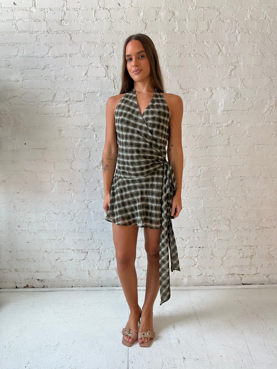 Woman wearing olive green abstract mini dress with wrap skirt detail and halter neckline. 