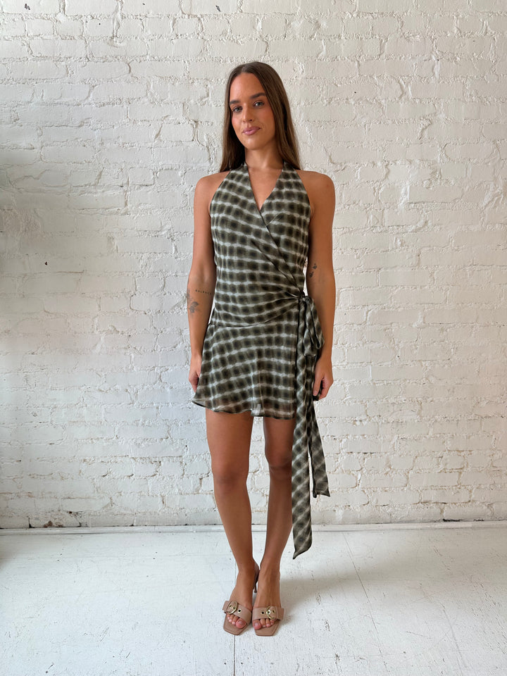 Woman wearing olive green abstract mini dress with wrap skirt detail and halter neckline. 