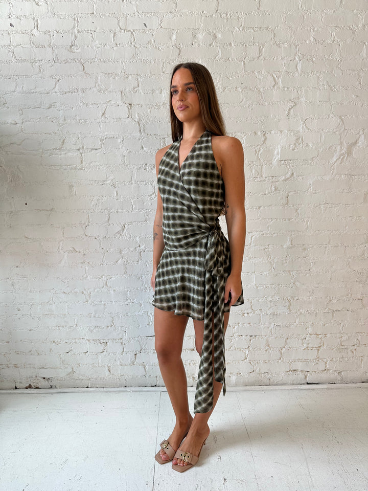 Woman wearing olive green abstract mini dress with wrap skirt detail and halter neckline. 