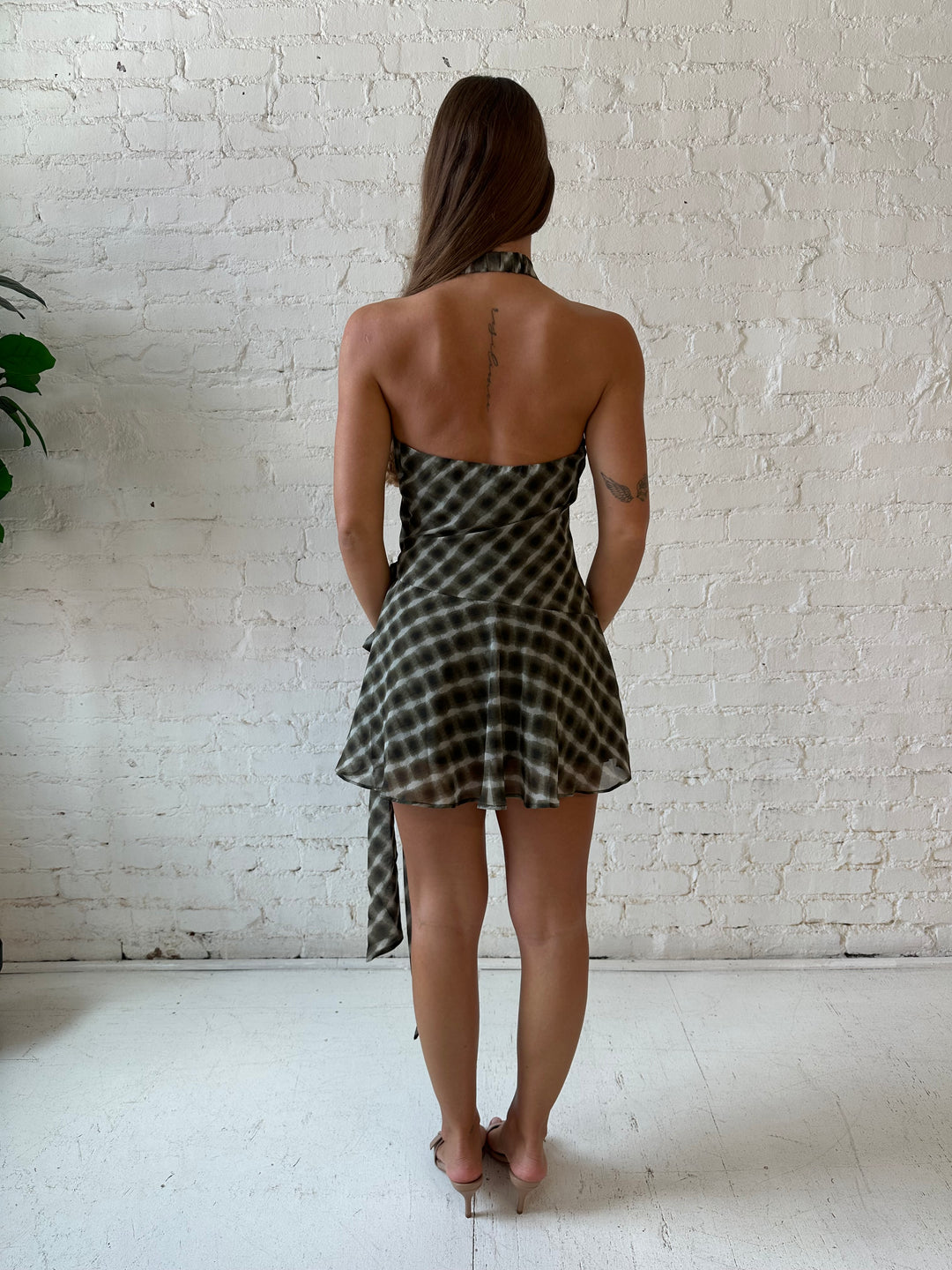 Woman wearing olive green abstract mini dress with wrap skirt detail and halter neckline. 