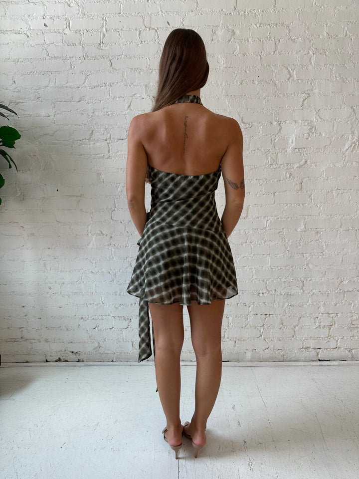 Woman wearing olive green abstract mini dress with wrap skirt detail and halter neckline. 