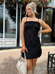 Woman wearing black floral textured mini dress with ruffle hem detail. 
