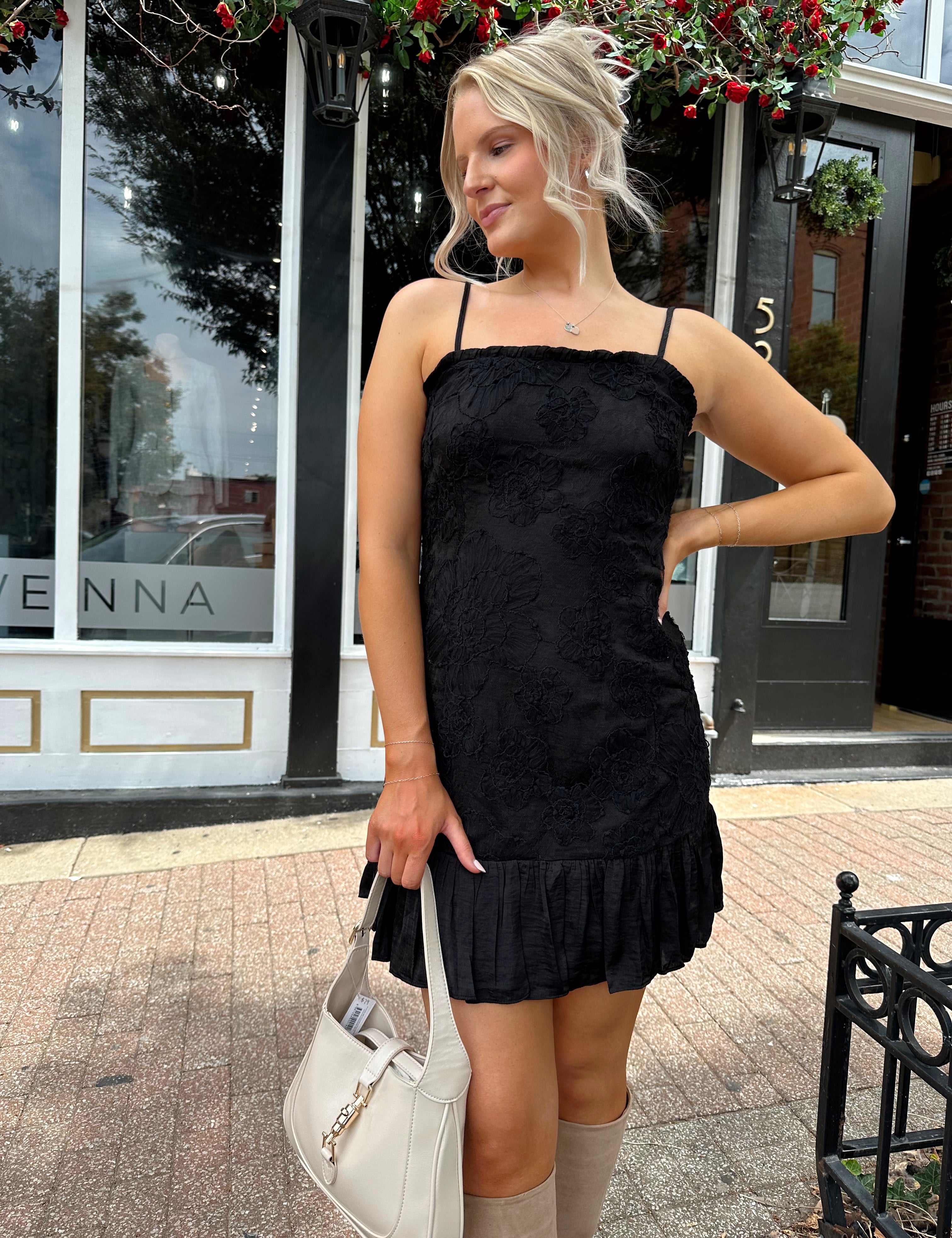 Woman wearing black floral textured mini dress with ruffle hem detail. 