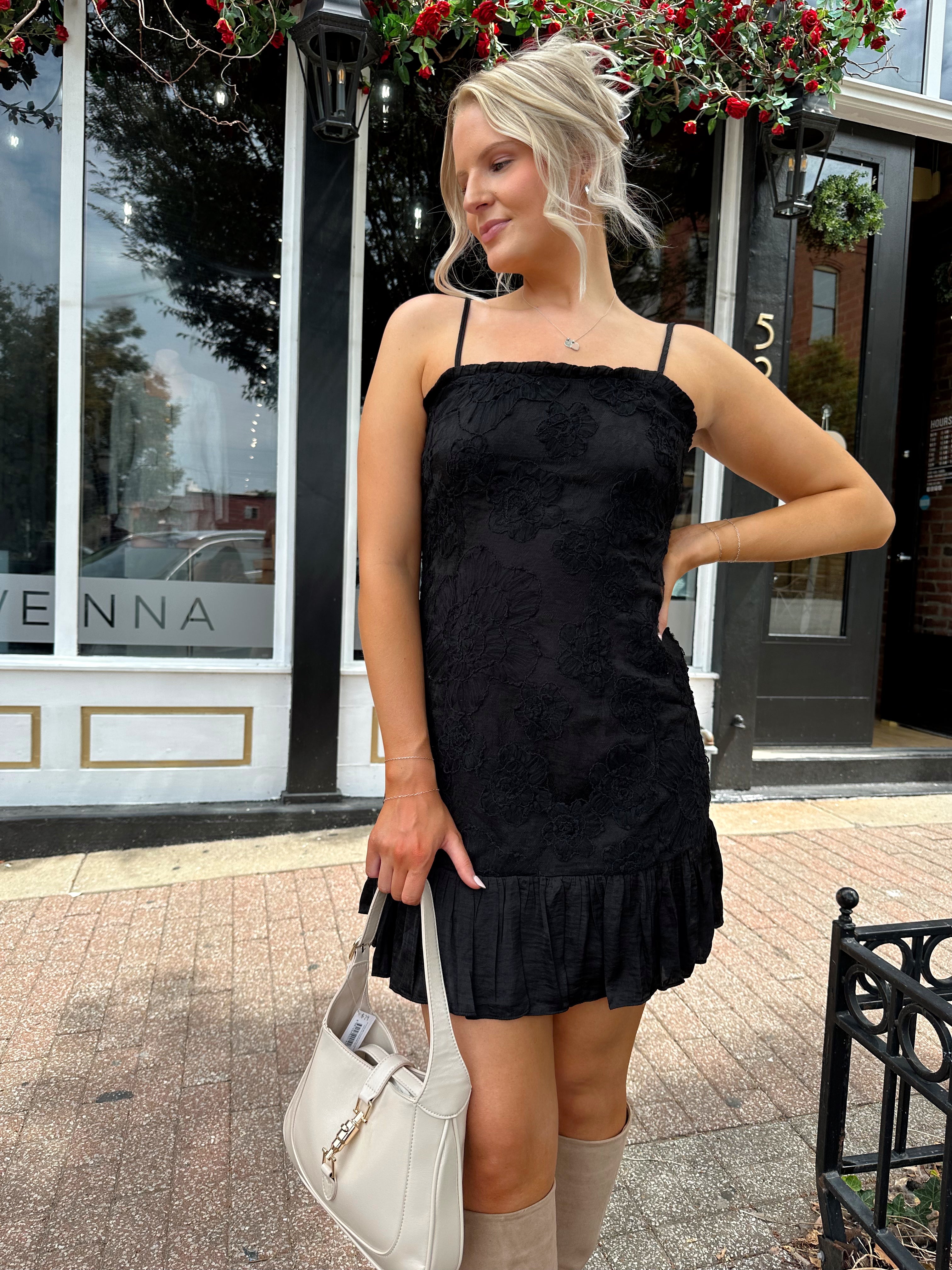 Woman wearing black floral textured mini dress with ruffle hem detail. 
