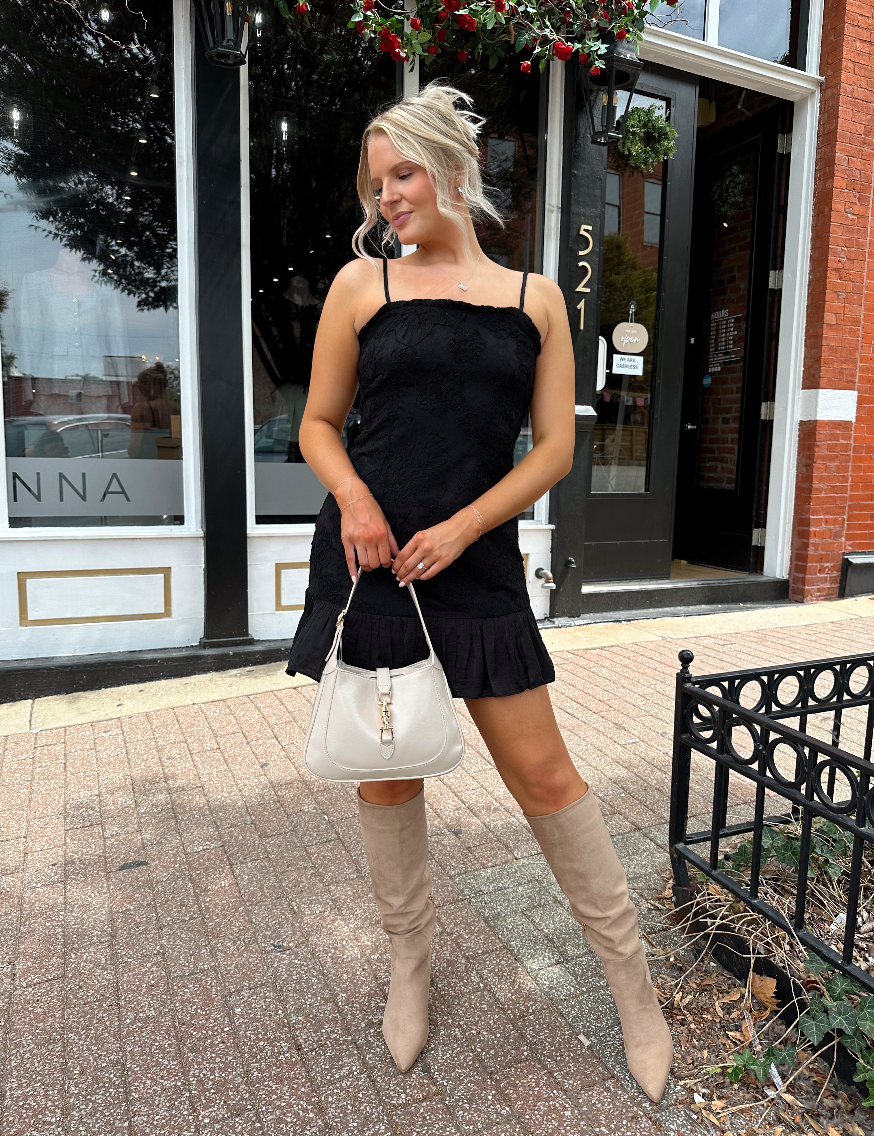 Woman wearing black floral textured mini dress with ruffle hem detail. 